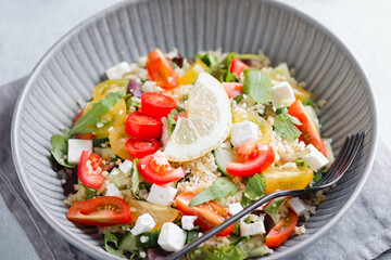 Salad with bulgur, cherry tomatoes, feta cheese and green herbs on concrete table top. Middle Eastern tabbouleh salad, top view