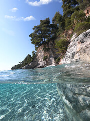 Fototapeta na wymiar Underwater and sea level photo of amazing tropical rocky turquoise clear seascape with caves and natural pine trees