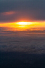 Fototapeta na wymiar Hight shot from airplane of sun setting above fluffy clouds 