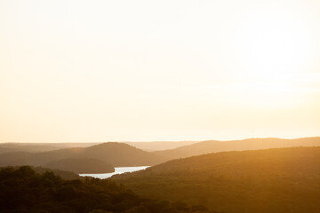 High view of the sun setting over a small lake and rolling hills