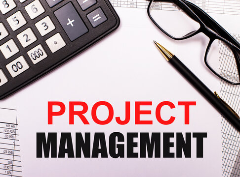 PROJECT MANAGEMENT is written in red and black on a white background next to a calculator, pen and black-framed glasses. Business concept