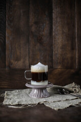 Cup of coffee on wooden table. Barraquito coffee in a small transparent cup on a ceramic stand. Dark brown wooden background. Drink in layers.