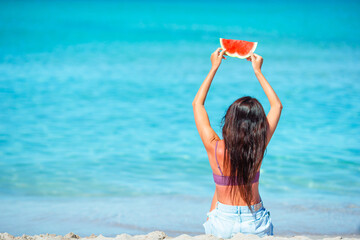 Happy girl having fun on the beach and eating watermelon