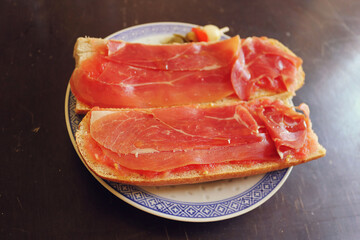 andalusian breakfast with bread, ham and tomato on a dish - picture of a toast of a mediterranean diet with a wooden table in the background