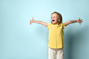 Little female in yellow t-shirt and white pants. She spreading her hands wide apart and screaming, posing on turquoise background. Close up