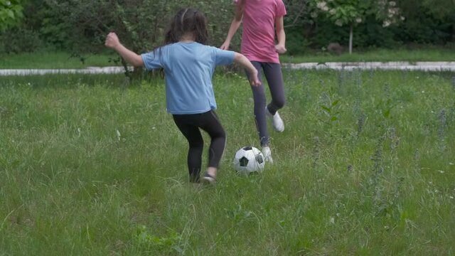 Children play with a ball for football. Cheerful little sisters play football on a green lawn.