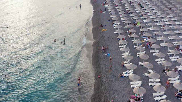 Rows of reed umbrellas at the sandy beach in Canj, on the Adriatic coast of Montenegro. People on vacation under sunshades, or in blue and turquoise sea. Impact of coronavirus pandemic on tourism.