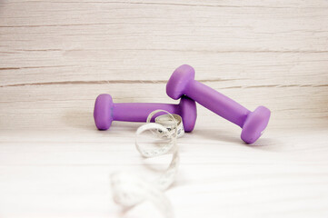 Health and fitness concept with purple dumbbells and centimeter on grey table, with copy space.
