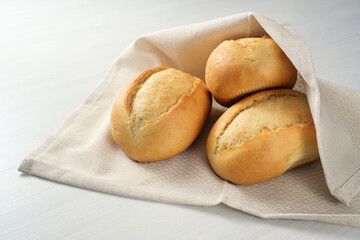 freshly baked bread rolls or buns from the baker in a kitchen towel on a white table, copy space, selected focus