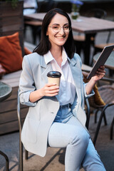 smiling businesswoman holding tablet and cofee at city cafe - 367621553