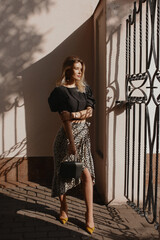 Gorgeous young woman with perfect blond hair in a fashionable skirt and blouse posing on the city street on a summer day