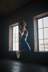 Fototapeta na wymiar Young athletic woman exercising using skipping rope in gym