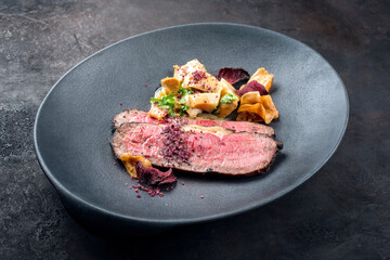 Modern style Commonwealth Sunday roast with sliced cold cuts roast beef, pickled mushrooms and vegetable chips offered as close-up on a cast-iron design plate