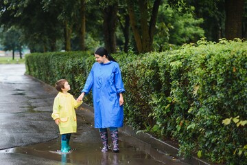 Fototapeta premium Mother with son walking in park in the rain wearing rubber boots