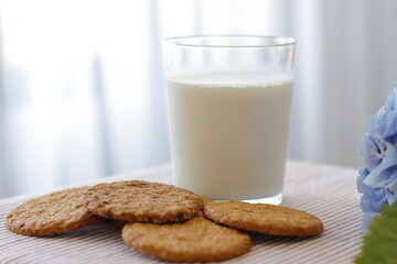 Oat cookies with glass of milk for breakfast on table cloth and blue flower on background, rustic healthy food 