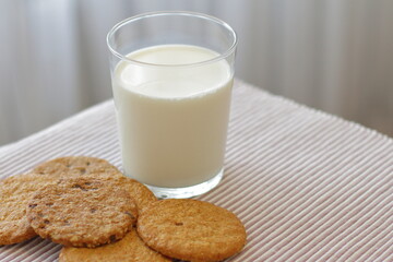 Oat cookies with glass of milk for breakfast on table cloth and blue flower on background, rustic healthy food 