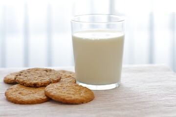 Oat cookies with glass of milk for breakfast on table cloth and blue flower on background, rustic healthy food 