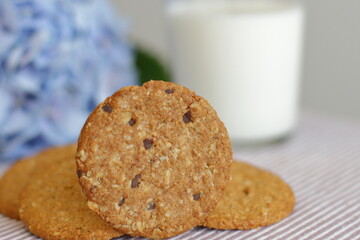 Oat cookies with glass of milk for breakfast on table cloth and blue flower on background, rustic healthy food 