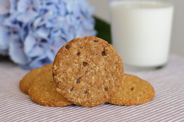 Oat cookies with glass of milk for breakfast on table cloth and blue flower on background, rustic healthy food 