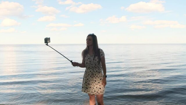 Happy woman having a video call using smartphone and monopod on sea horizon at sunset background