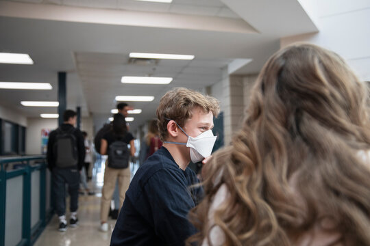 High School Boy In Flu Mask With Friends In Corridor