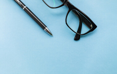 Glasses and a pen are on the table. Close up top view of pen and glasses on blue background for mockup design modern lifestyle stationary concept. Blue office desk with supplies. Space for your text.