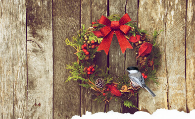 Christmas wreath with natural decorations hung on a wooden wall with a chickadee perched.