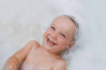 emotional Baby Toddler lies washed in the bathroom with foam and laughs