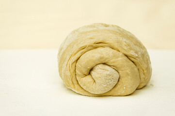 Yeast dough formed into a bun roll on the kitchen table sprinkled with flour with selective focus on the curls of the bagel. 
