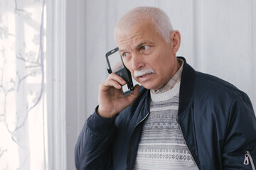elderly man on phone. gray-haired man listening to conversation with frown. Beautiful grandfather...