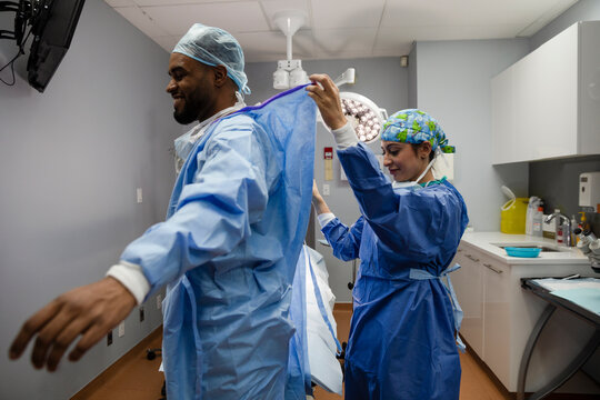 Surgeon helping colleague with surgical gown in operating room