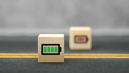 cube with full charged battery symbol and a cube out of focus with low energy symbol on asphalt surface