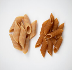 Raw and cooked dark wholemeal pasta on a white background
