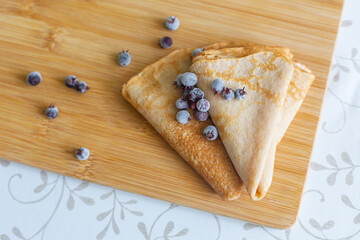 Two pancakes and frozen shadberry berries on a cutting board, top view. Traditional cuisine, homemade food, dessert, pastries. Frozen products.