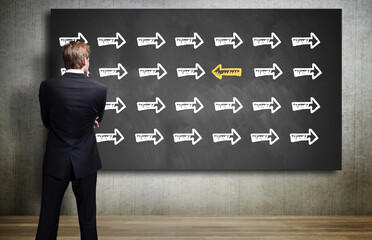 businessman looking at a chalkboard with an arrow symbol that is different from all others