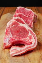 Fresh uncooked lamb loin chops on a wooden board, black background, Close up, Butcher craft concept. Vertical shot.