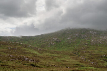Mountains peaks in clouds, Connemara region, West of Ireland.  Rough terrain with green grass. Cloudy moody sky.