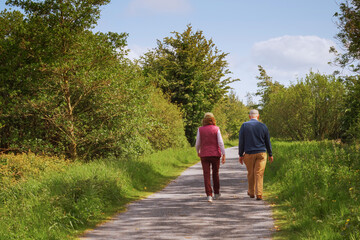 Old couple walking  on a foot path on a warm sunny day. Dressed in bright color clothes.