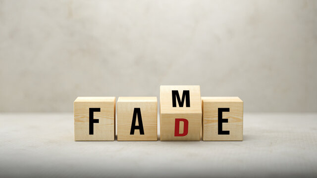 Fame or Fade concept with revolving letters on wooden cubes viewed low angle over a grey background with copyspace above
