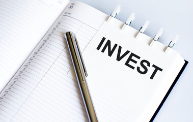text INVEST on the short note texture background with pen