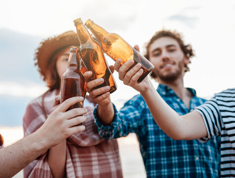 A group of happy friends clink their beer bottles, spending time relaxing on the beach