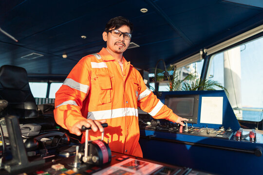 Filipino deck Officer on bridge of vessel or ship wearing coverall during navigaton watch at sea . He is maneuvering with cpp thrusters propulsion