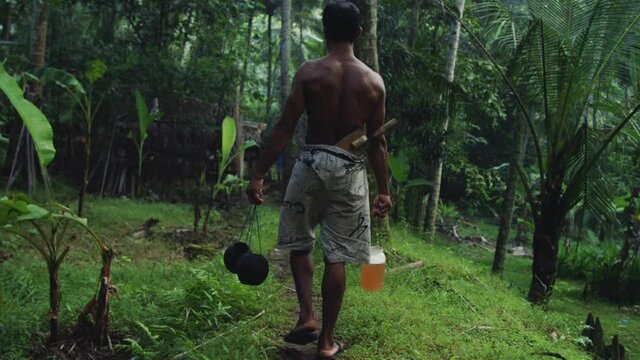 Farmer takes coconut nectar to grass hut in jungle permaculture farm in Bali