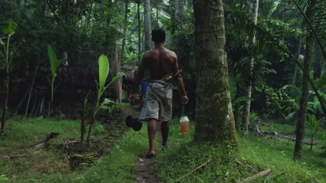 Farmer takes coconut nectar to grass hut in jungle permaculture farm in Bali