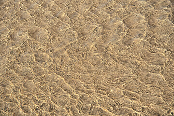 Surface of sea water with ripples on beach sand.