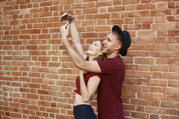 A couple makes a joint photo. The boy and girl makes selfie on phone. A young couple takes selfie