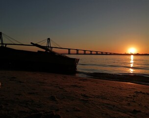 Canoa en la playa, atardecer en la costa del río y puente