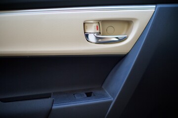 Obraz na płótnie Canvas interior view of car door handle. also electronic window release button can be seen. the interior is beige and black.