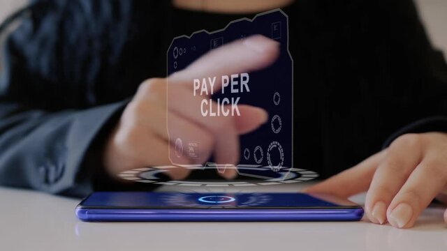Female hand interacts HUD hologram with text Pay per click. Woman in black uses conceptual holographic technology of the future on the screen of a smartphone lying on a table