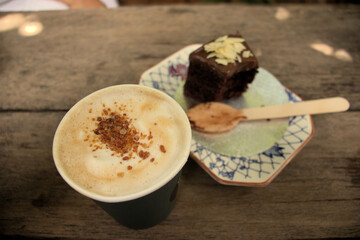 Latte coffee with sugar granules on top served with chocolate cake and almond slithers